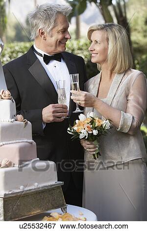 Stock Photo - Middle-aged couple toasting near wedding cake, portrait. Fotosearch