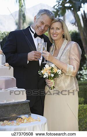Stock Photo - Middle-aged couple toasting near wedding cake, portrait. Fotosearch