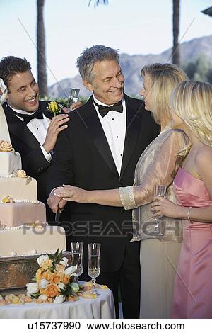 Stock Image - Middle-aged couple with young man and woman gathered near wedding cake. Fotosearch