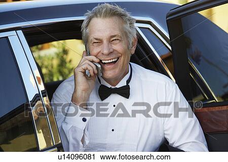 Stock Image - Middle-aged man talking on mobile phone in open door of limousine, portrait. Fotosearch