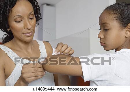 Mother applying bandaid to daughter (7-9) indoors View Large Photo Image Picture - Mother applying bandaid to daughter (7-9) indoors. Fotosearch
