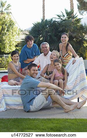 Stock Photo - Multigenerational family with two girls and boy sitting on deck chair by swimming pool, portrait. Fotosearch