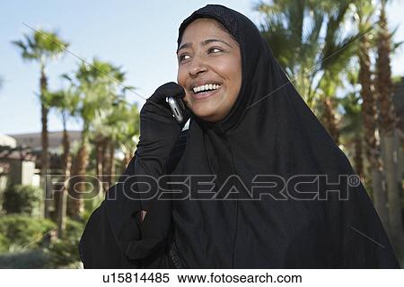 Stock Photography - Muslim woman in black hijab talking on mobile, laughing. Fotosearch