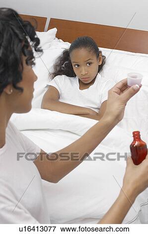 Stock Photo - Nurse pouring medication for girl (7-9) lying in bed. Fotosearch