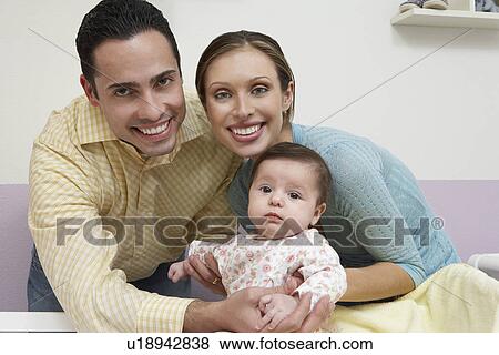 Stock Photo - Parents with baby (1-6 months) at home, portrait. Fotosearch