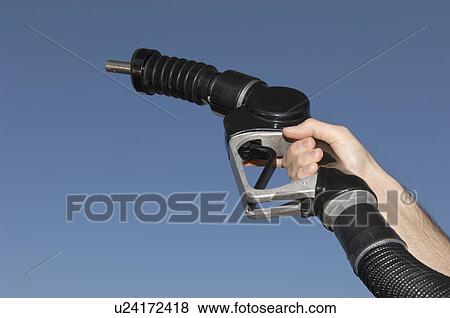 Stock Photo - Person holding fuel pump against blue sky, close-up. Fotosearch