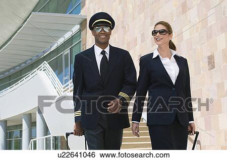 Stock Photograph - Pilot and flight attendant walking outside building. Fotosearch