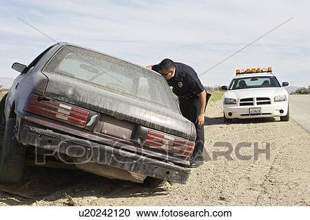Stock Image - Police officer looking into abandoned car on roadside. Fotosearch