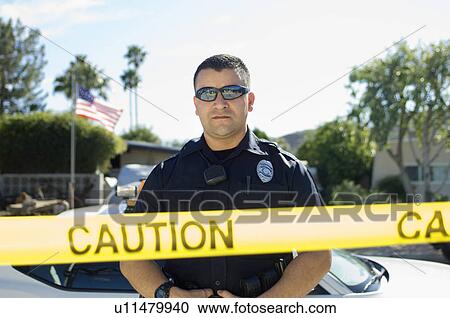 Stock Image - Police Officer Standing Behind Police Tape. Fotosearch