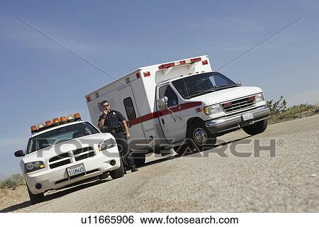 Police officer standing by police car and ambulance View Large Photo Image Stock Photograph - Police officer standing by police car and ambulance. Fotosearch