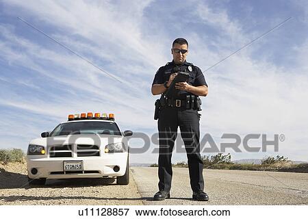 Stock Photo - Police officer taking notes in front of police car. Fotosearch