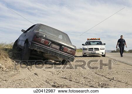 Stock Photo - Police officer walking towards abandoned car on roadside. Fotosearch