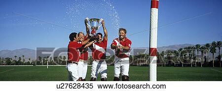 Stock Photography - Polo team celebrating with trophy on field. Fotosearch