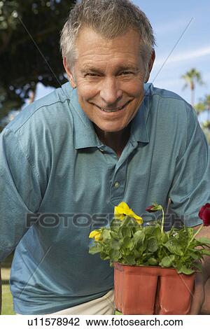Stock Image - Portrait of man with flowers in garden. Fotosearch