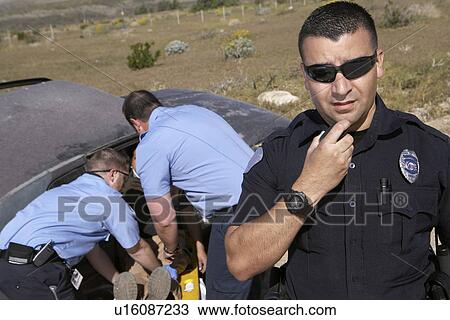 Portrait of police officer, paramedics rescuing car accident victim in background View Large Photo Image Stock Image - Portrait of police officer, paramedics rescuing car accident victim in background. Fotosearch
