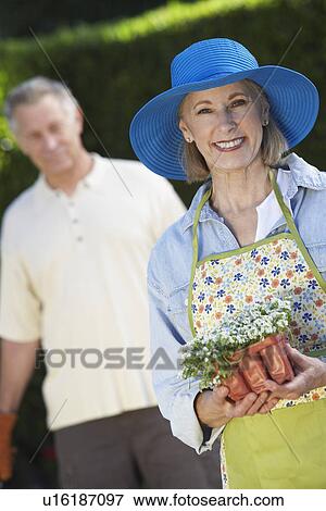 Stock Photo - Portrait of senior woman with flowers, out of focus man in background. Fotosearch