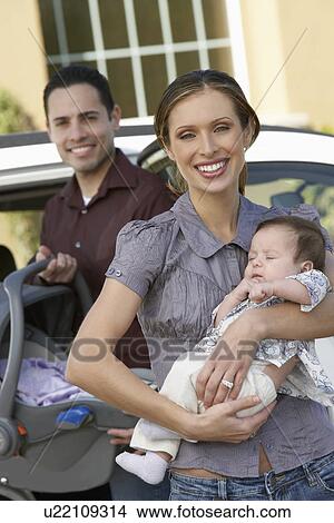Portrait of woman with baby (1-6 months) by car, man in background View Large Photo Image Picture - Portrait of woman with baby (1-6 months) by car, man in background. Fotosearch