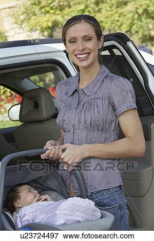 Stock Photo - Portrait of woman with baby (1-6 months) in carrier by car. Fotosearch