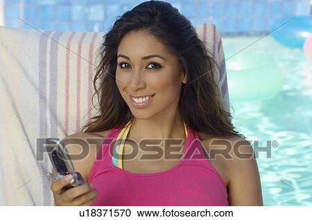 Stock Image - Portrait of woman with mobile phone at swimming pool. Fotosearch