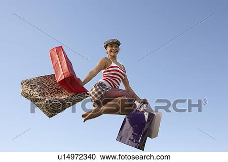 Stock Image - Portrait of young woman jumping with shopping bags. Fotosearch
