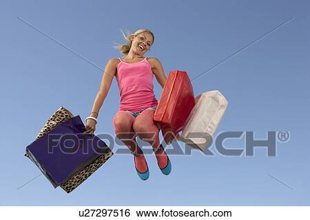 Stock Photograph - Portrait of young woman jumping with shopping bags. Fotosearch