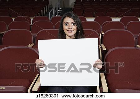 Stock Image - Portrait of young woman with blank placard, smiling. Fotosearch
