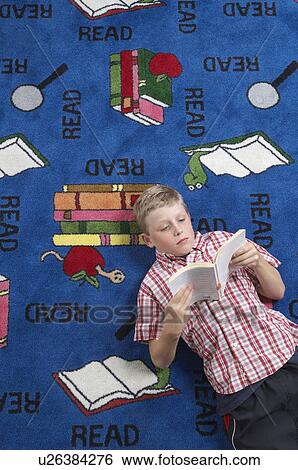 Stock Photograph - School boy reading book on floor in library. Fotosearch
