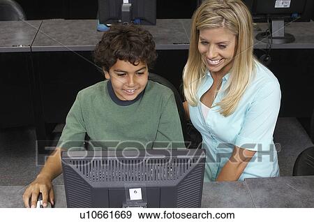 Stock Photo - School boy using computer with teacher in classroom. Fotosearch