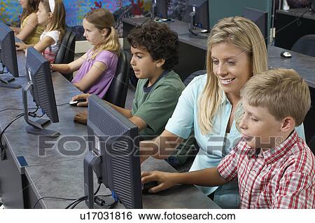 Stock Photograph - School children using computers with teacher in classroom. Fotosearch