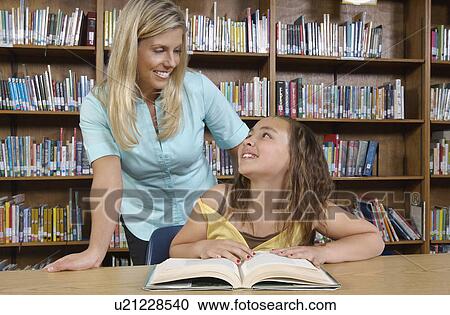School girl reading book with teacher in library View Large Photo Image Stock Image - School girl reading book with teacher in library. Fotosearch