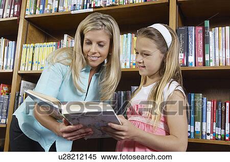 Stock Photography - School girl reading book with teacher in library. Fotosearch