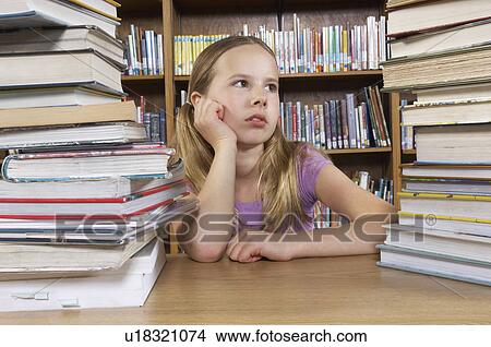 Picture - School girl sitting at desk with books in library. Fotosearch