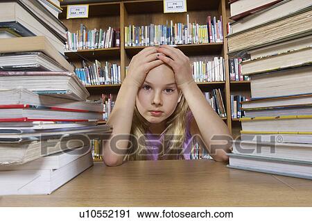 Stock Image - School girl sitting at desk with books in library, portrait. Fotosearch