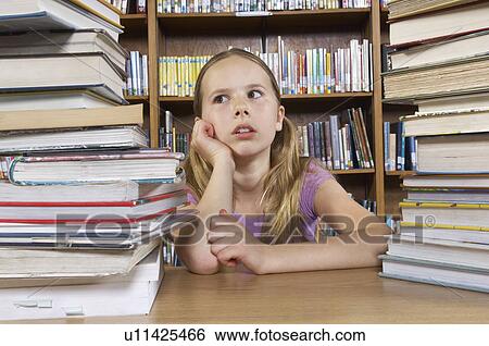 Stock Photograph - School girl sitting at desk with books in library. Fotosearch