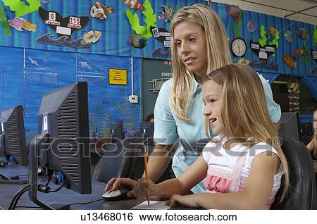 Stock Photograph - School girl using computer with teacher in classroom. Fotosearch