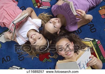 Stock Photo - School girls reading books on floor in library. Fotosearch