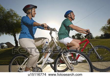 Picture - Senior couple cycling in park at dusk. Fotosearch