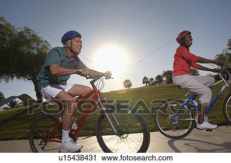 Stock Image - Senior couple cycling in park at dusk. Fotosearch