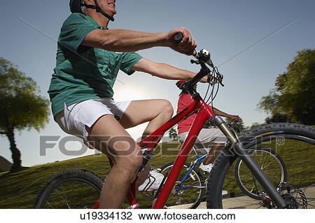 Stock Image - Senior couple cycling in park at dusk. Fotosearch