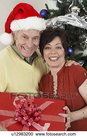Senior couple holding present in front of Christmas tree View Large Photo Image Stock Image - Senior couple holding present in front of Christmas tree. Fotosearch