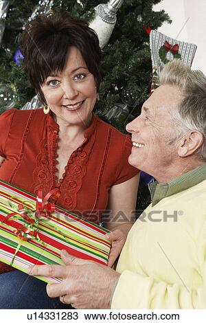 Senior couple holding present in front of Christmas tree View Large Photo Image Stock Image - Senior couple holding present in front of Christmas tree. Fotosearch
