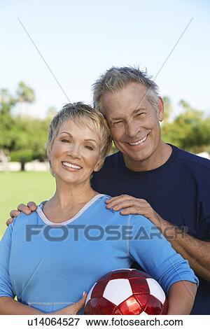 Stock Photo - Senior couple holding soccer ball in park, portrait. Fotosearch