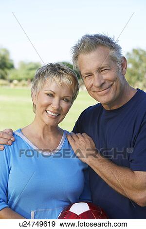 Stock Photo - Senior couple holding soccer ball in park, portrait. Fotosearch