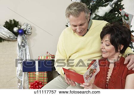 Stock Photo - Senior couple looking at Christmas card in front of decorations. Fotosearch
