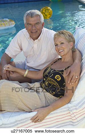 Senior couple sitting on deck chair by swimming pool, portrait View Large Photo Image Stock Photography - Senior couple sitting on deck chair by swimming pool, portrait. Fotosearch