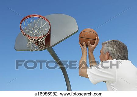 Stock Image - Senior man aiming basketball at hoop, outdoors. Fotosearch