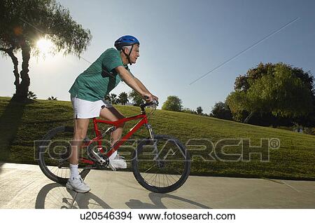 Picture - Senior man cycling in park at dusk, side view. Fotosearch