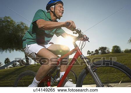 Stock Photography - Senior man cycling in park at dusk. Fotosearch