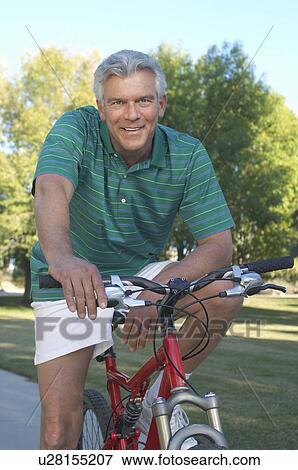Stock Photo - Senior man on bicycle in park, portrait. Fotosearch