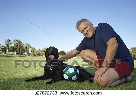 Senior man petting dog beside soccer ball in park View Large Photo Image Stock Image - Senior man petting dog beside soccer ball in park. Fotosearch